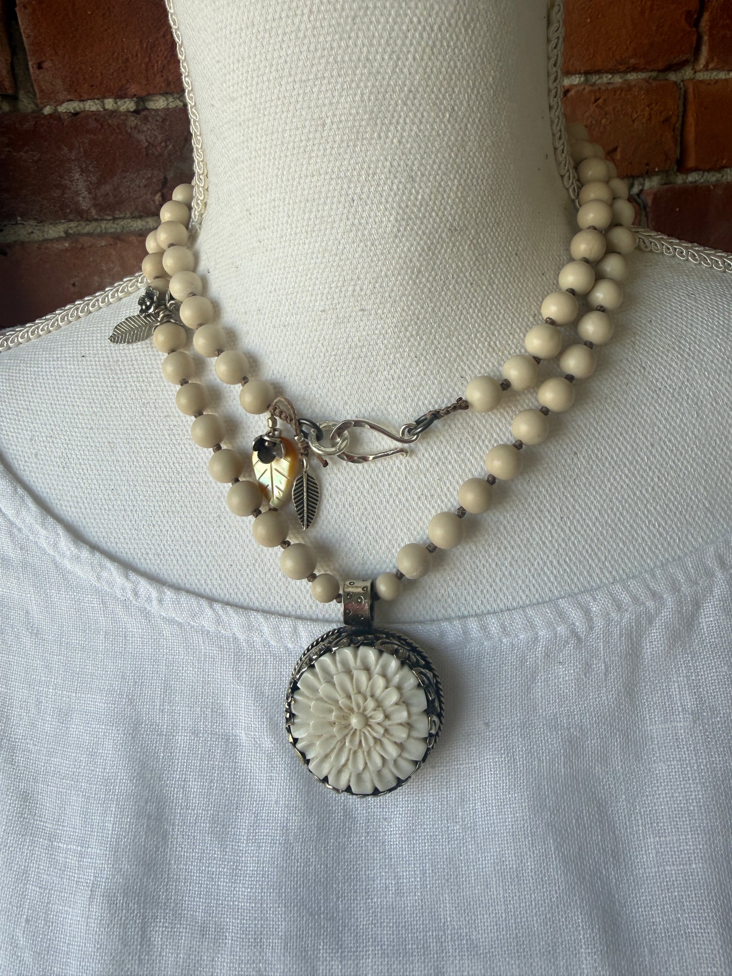 Tibetan carved bone dahlia pendant on hand knotted riverstone beads necklace. Fine silver flower cluster and MOP leaf dangles.