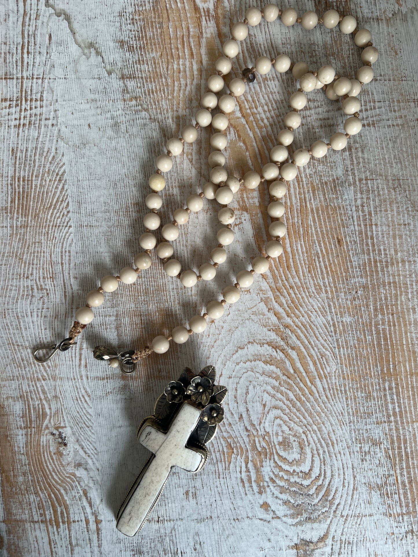 Bone cross with floral accents on creamy riverstone beads. Hand knotted long necklace.