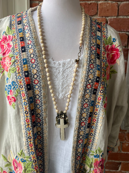 Bone cross with floral accents on creamy riverstone beads. Hand knotted long necklace.