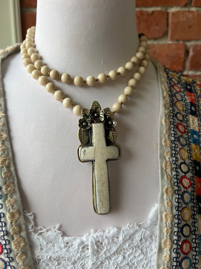 Bone cross with floral accents on creamy riverstone beads. Hand knotted long necklace.