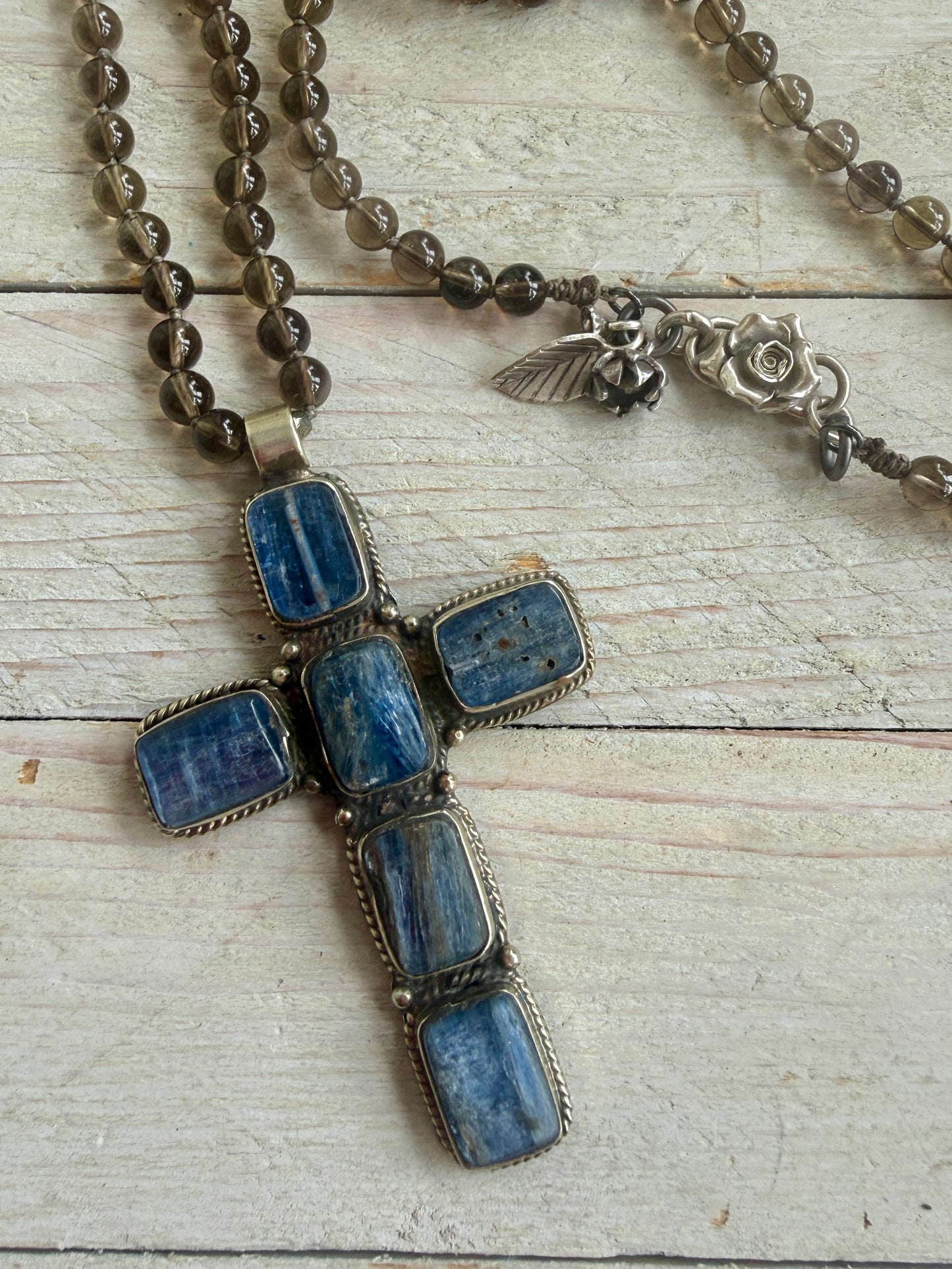 Blue kyanite cross on knotted smoky quartz necklace with fine silver flower accents.
