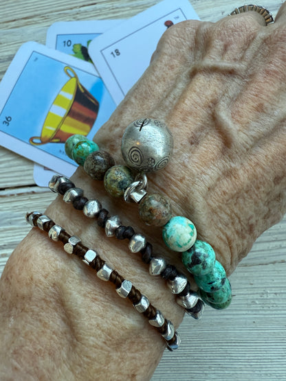 Turquoise beads surround a Karen Hill Tribe bell bead made of fine silver for this stretch bracelet. 6-5-7”.