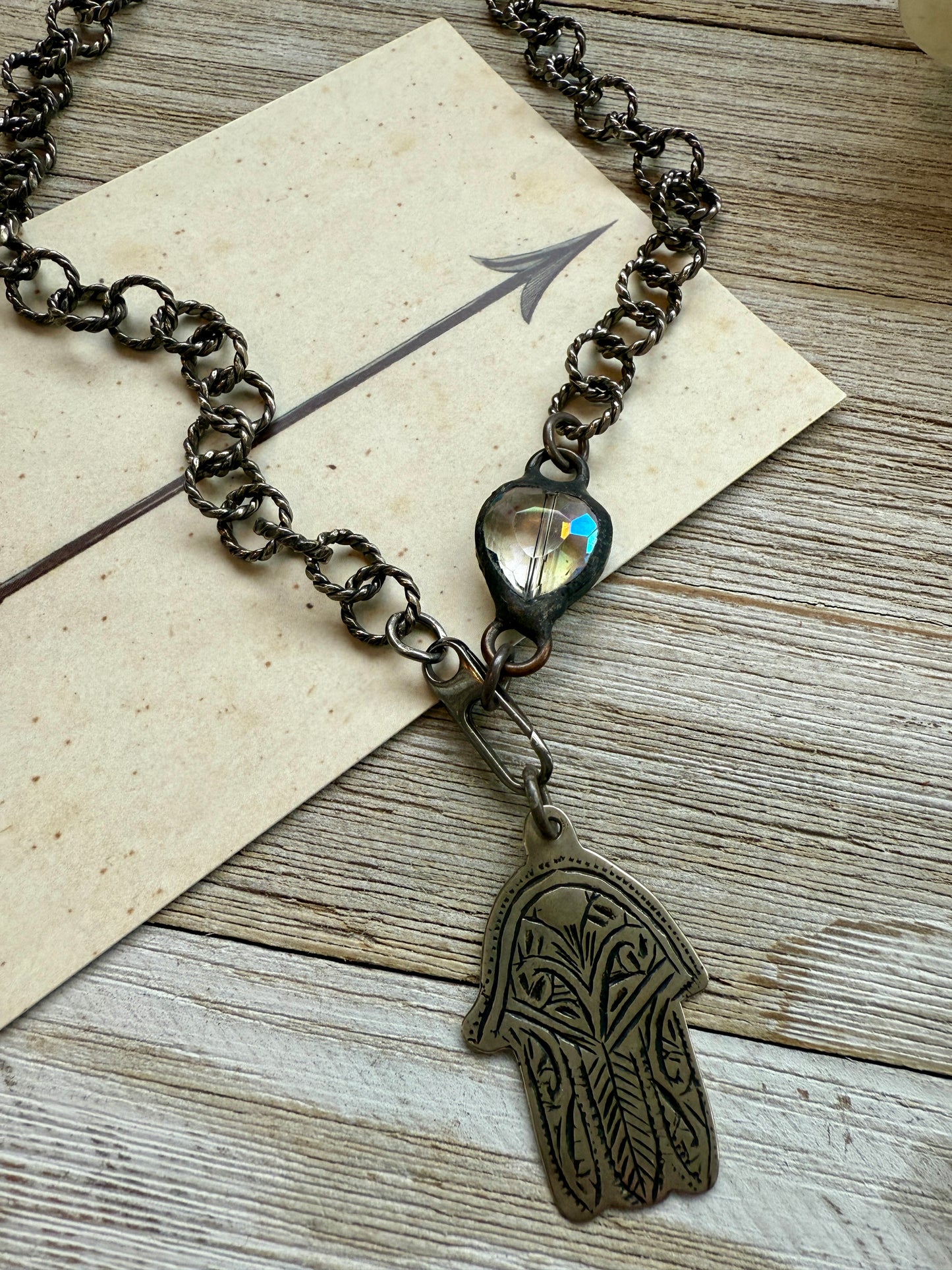 Chunky oxidized sterling rope chain with a crystal hear, sterling carabiner clasp, and stamped bronze hamsa pendant. 18”