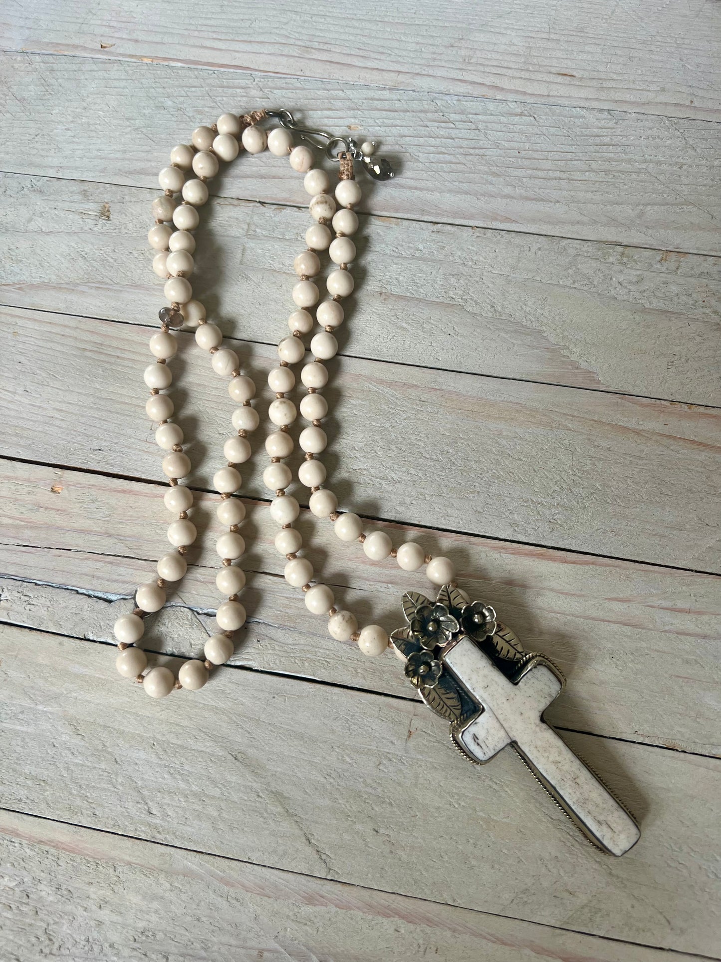 Bone cross with floral accents on creamy riverstone beads. Hand knotted long necklace.