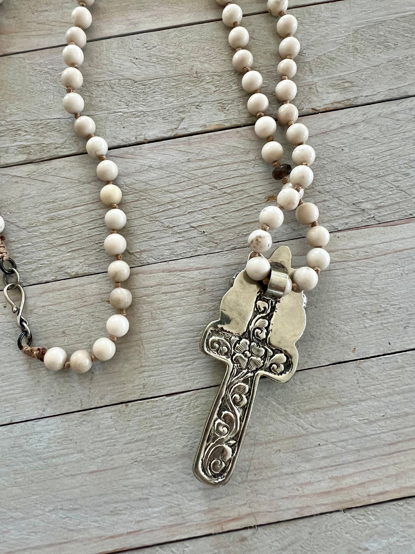 Bone cross with floral accents on creamy riverstone beads. Hand knotted long necklace.