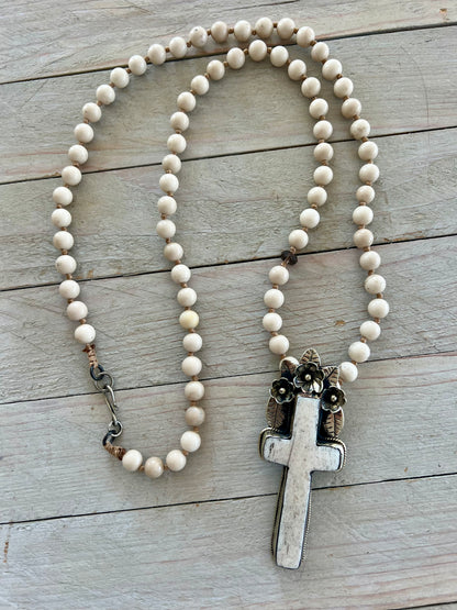 Bone cross with floral accents on creamy riverstone beads. Hand knotted long necklace.