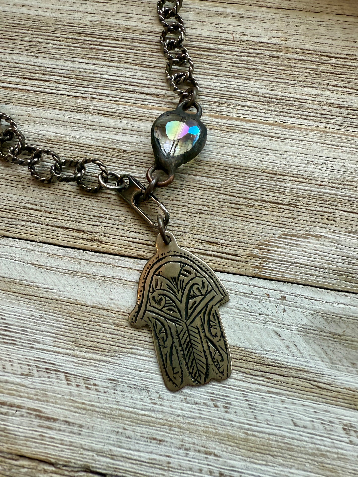 Chunky oxidized sterling rope chain with a crystal hear, sterling carabiner clasp, and stamped bronze hamsa pendant. 18”