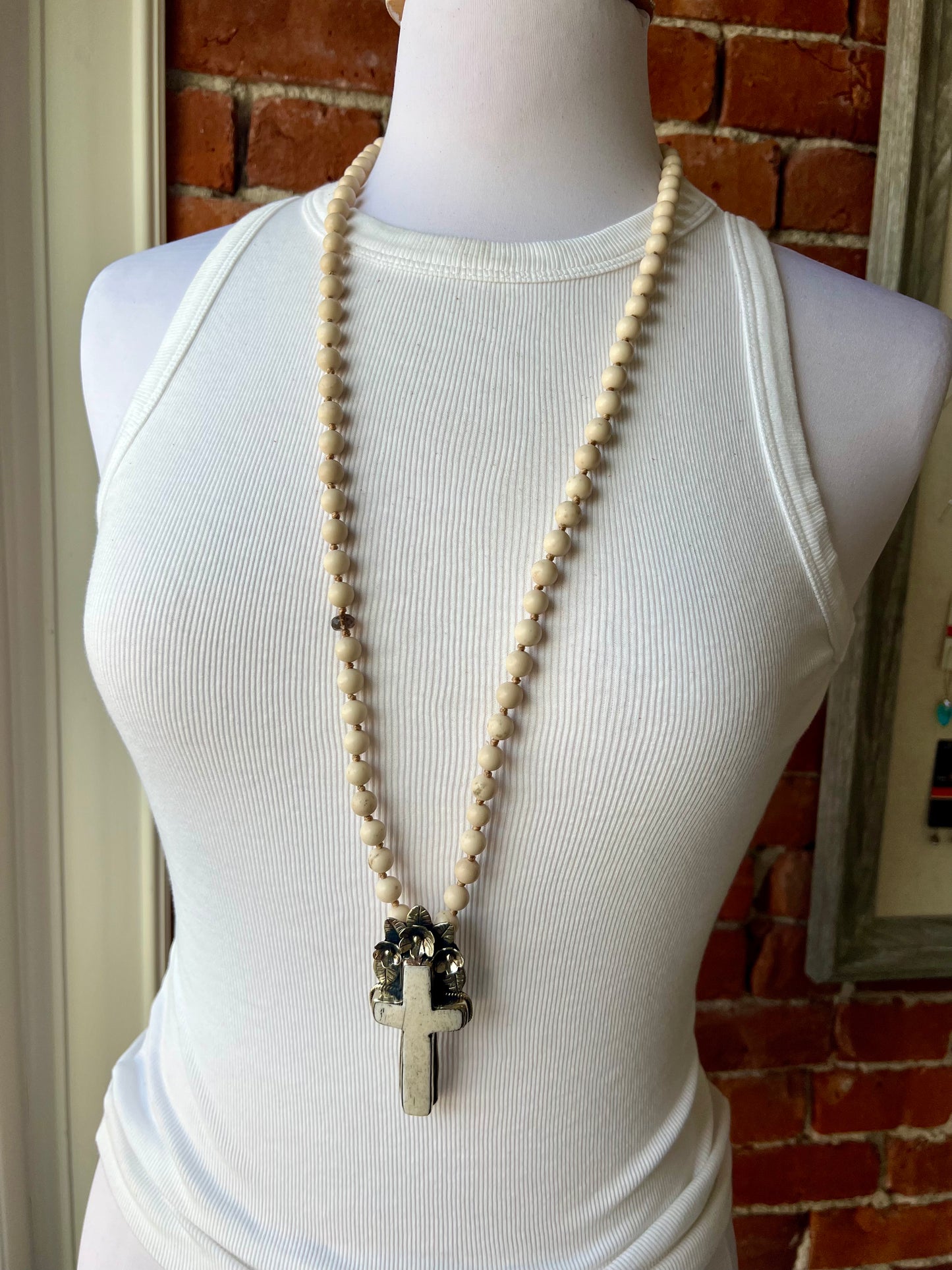 Bone cross with floral accents on creamy riverstone beads. Hand knotted long necklace.