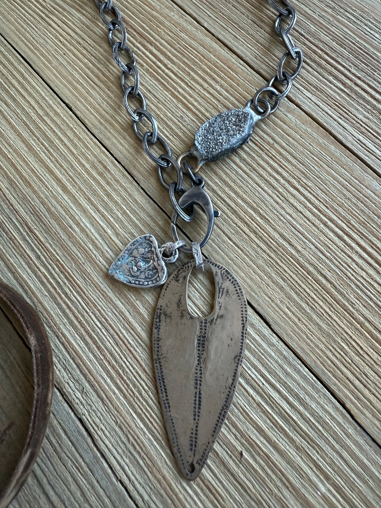 A rustic bronze shield hangs from an oxidized sterling chain. A sterling heart and pyrite add interest. Oxidized sterling lobster clasp allows you to change pendants out and adjust length. 19”