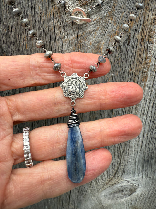 Wire wrapped blue kyanite with a sterling silver religious medal connector on grey silverite chain necklace. 28” chain additional 2.25” pendant and stone.