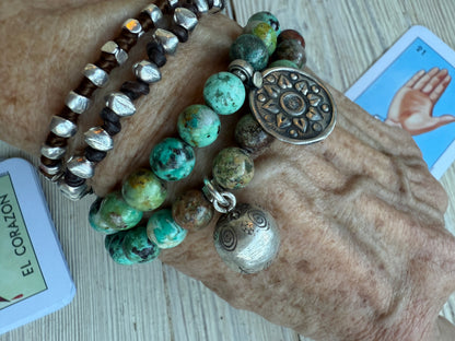 Turquoise beads surround a Karen Hill Tribe bell bead made of fine silver for this stretch bracelet. 6-5-7”.