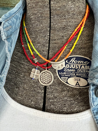 Primary colors surround a woven fine silver pendant necklace.