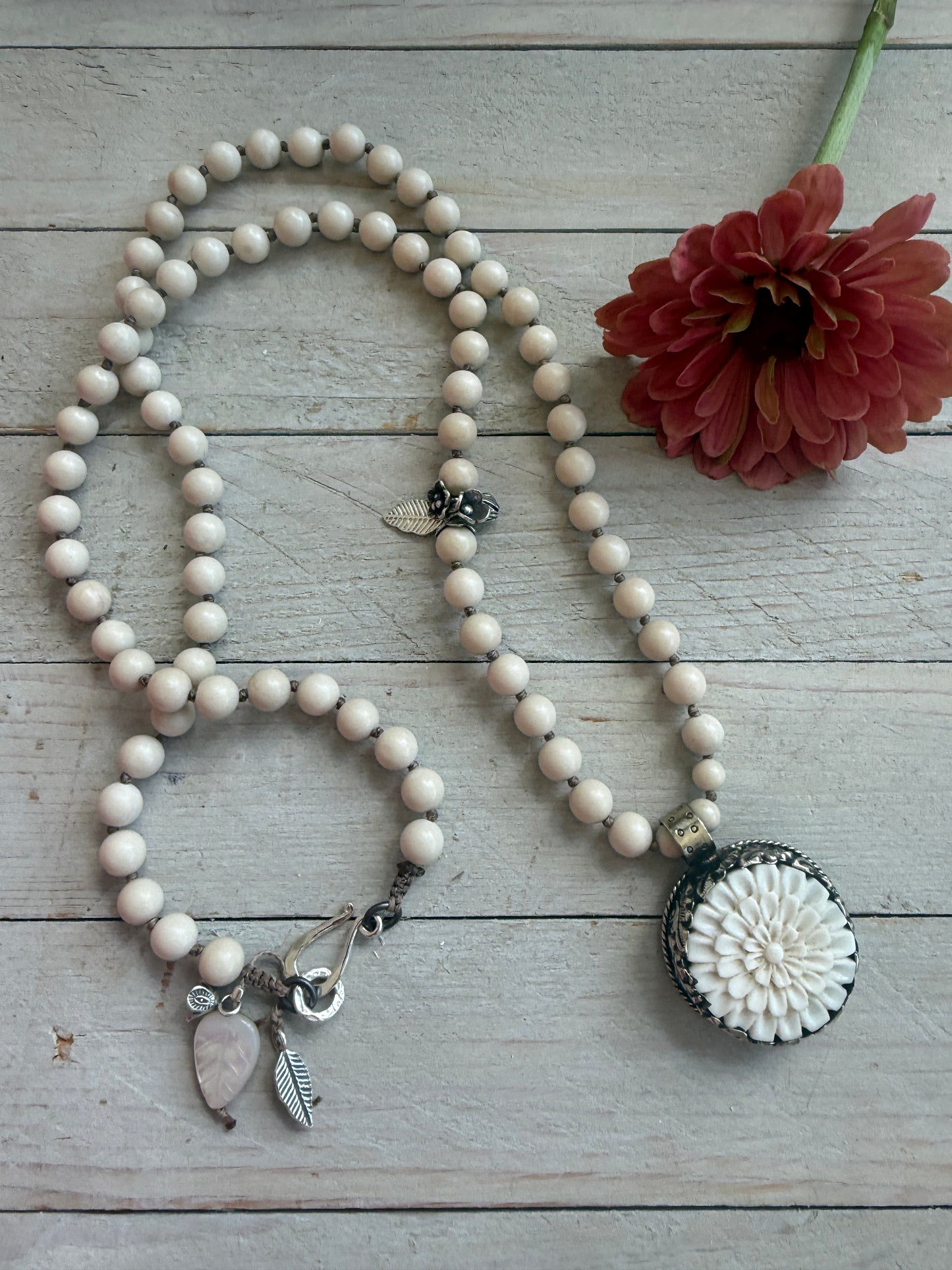 Tibetan carved bone dahlia pendant on hand knotted riverstone beads necklace. Fine silver flower cluster and MOP leaf dangles.