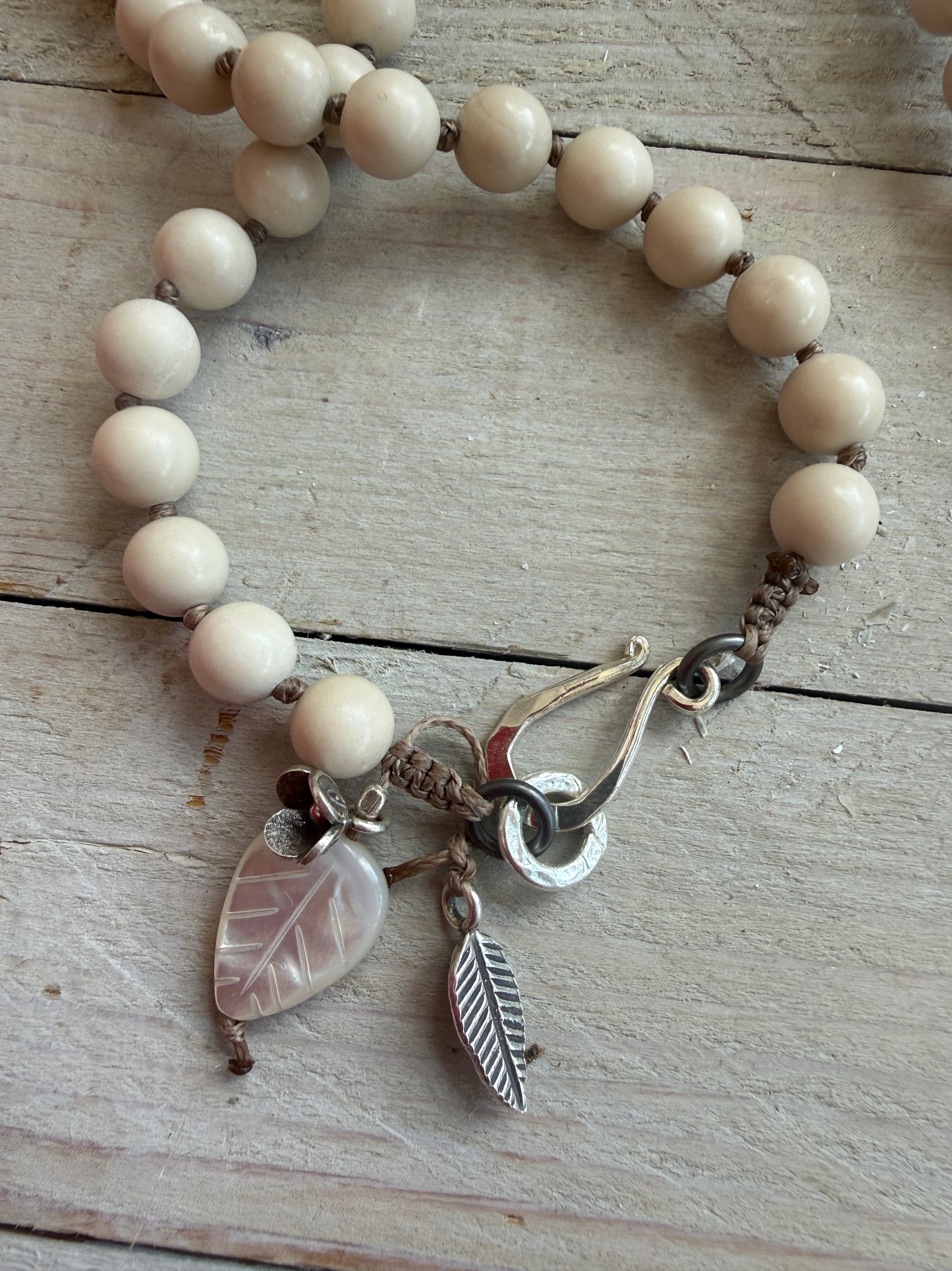 Tibetan carved bone dahlia pendant on hand knotted riverstone beads necklace. Fine silver flower cluster and MOP leaf dangles.