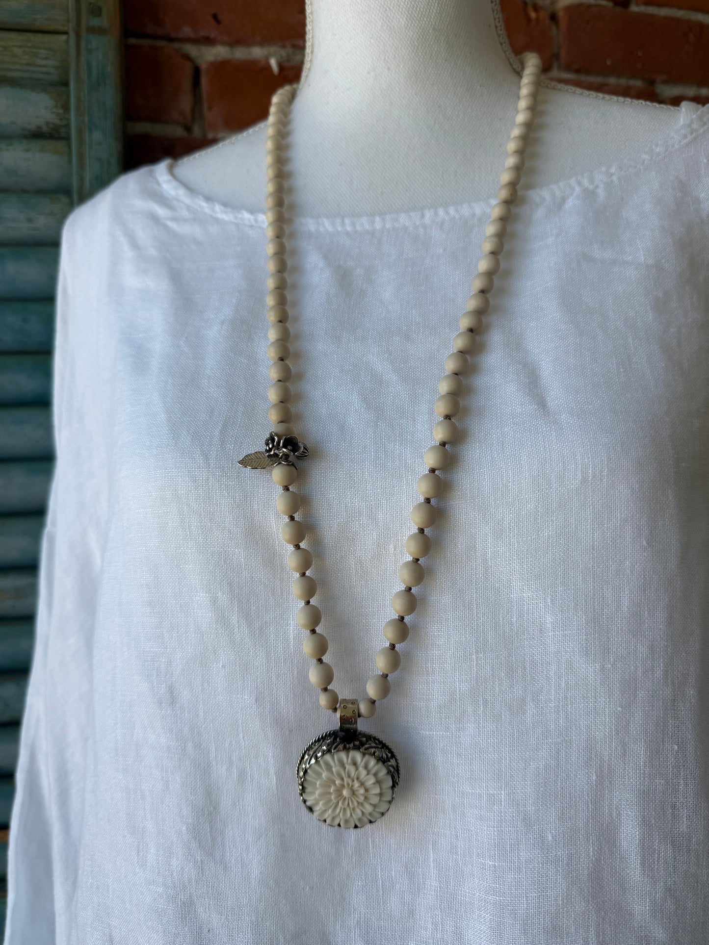 Tibetan carved bone dahlia pendant on hand knotted riverstone beads necklace. Fine silver flower cluster and MOP leaf dangles.