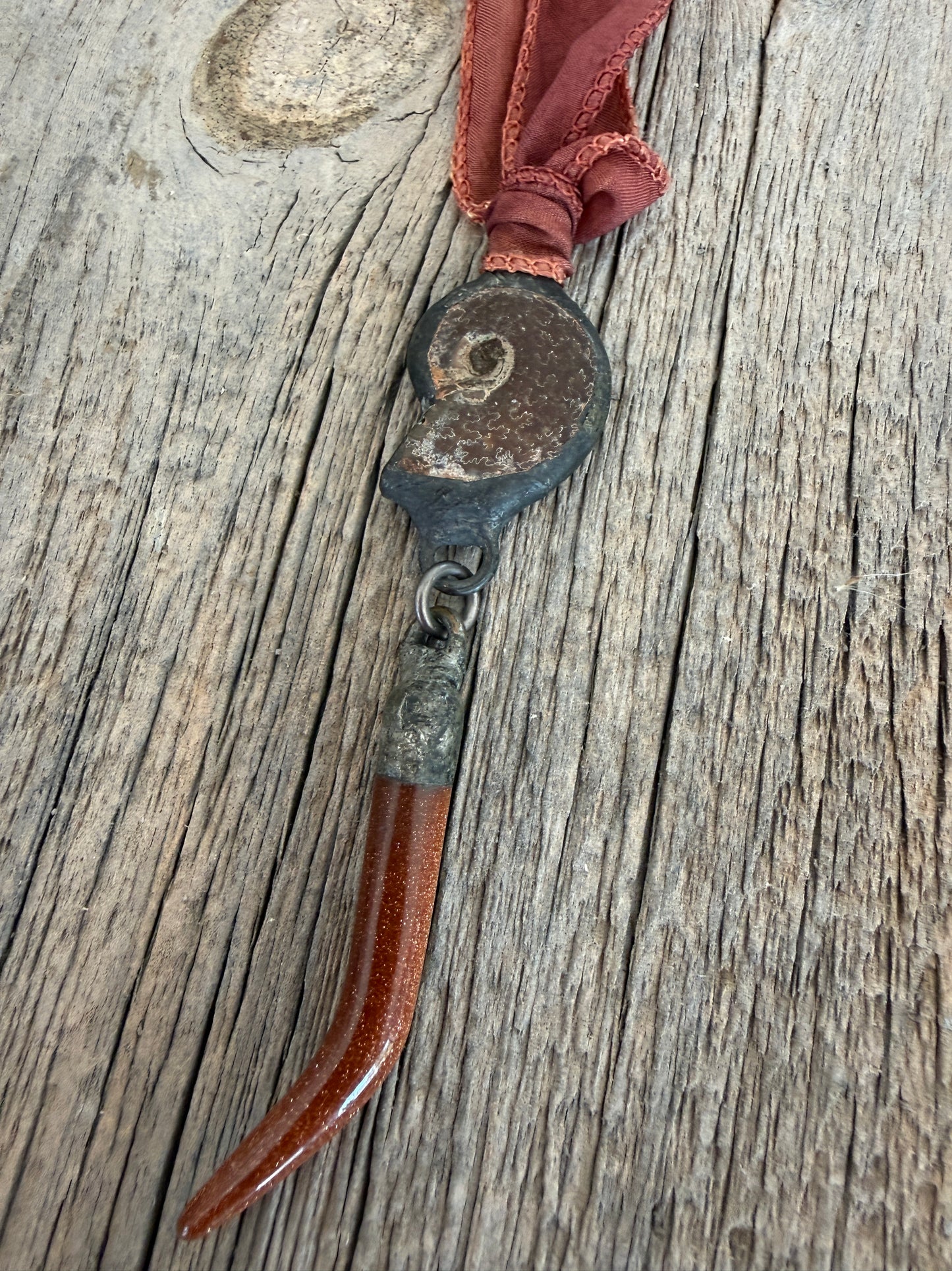 Ammonite and goldstone tusk on rust silk ribbon necklace. Adjustable to 36”