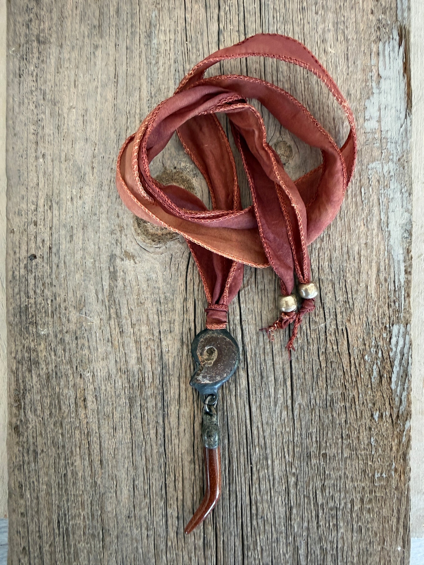 Ammonite and goldstone tusk on rust silk ribbon necklace. Adjustable to 36”