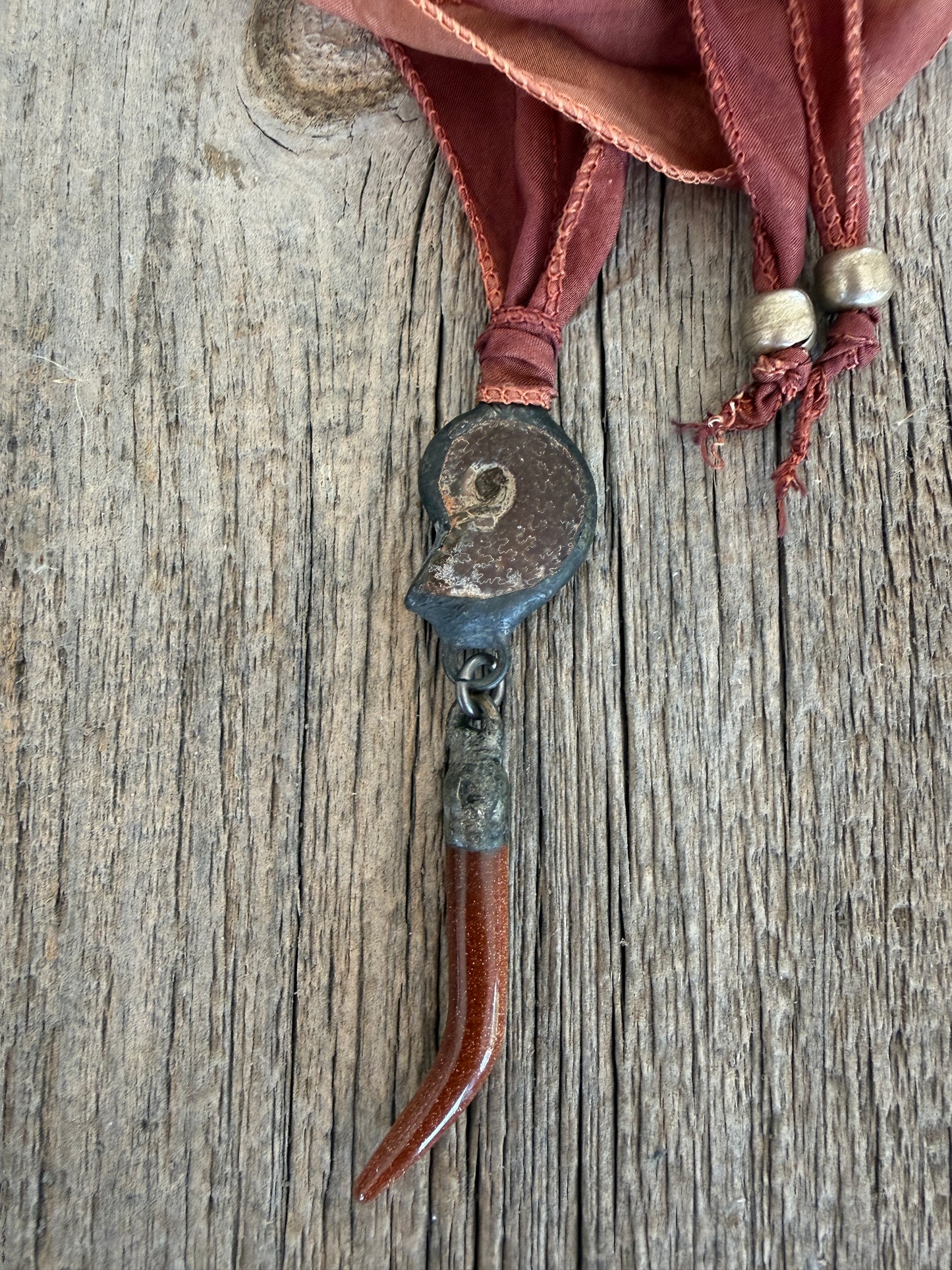 Ammonite and goldstone tusk on rust silk ribbon necklace. Adjustable to 36”