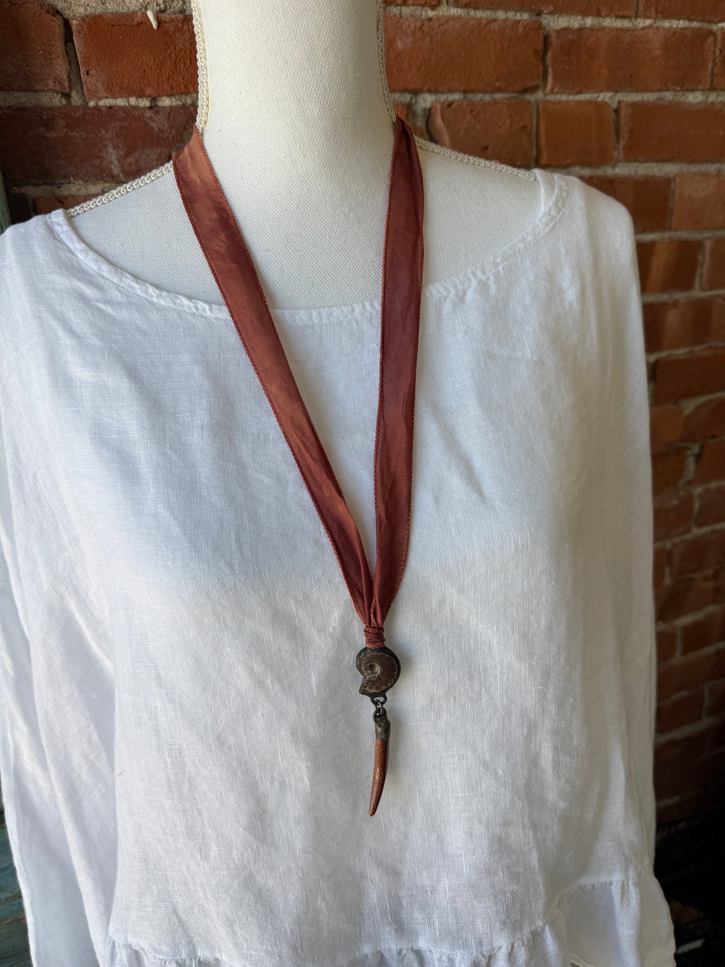 Ammonite and goldstone tusk on rust silk ribbon necklace. Adjustable to 36”