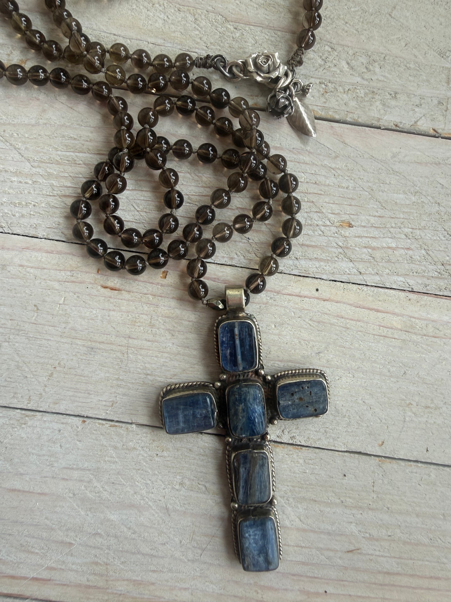 Blue kyanite cross on knotted smoky quartz necklace with fine silver flower accents.